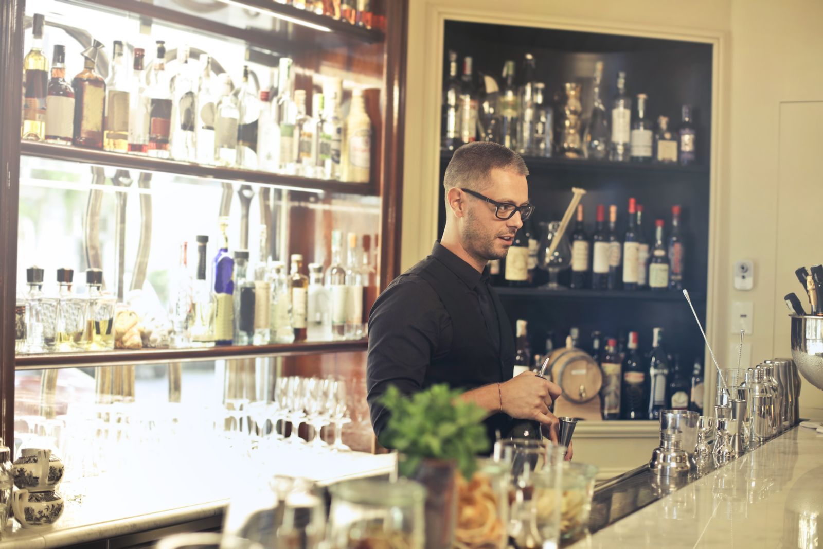 Le barman du Cardinal derrière le comptoir, devant l'étagère de bouteilles