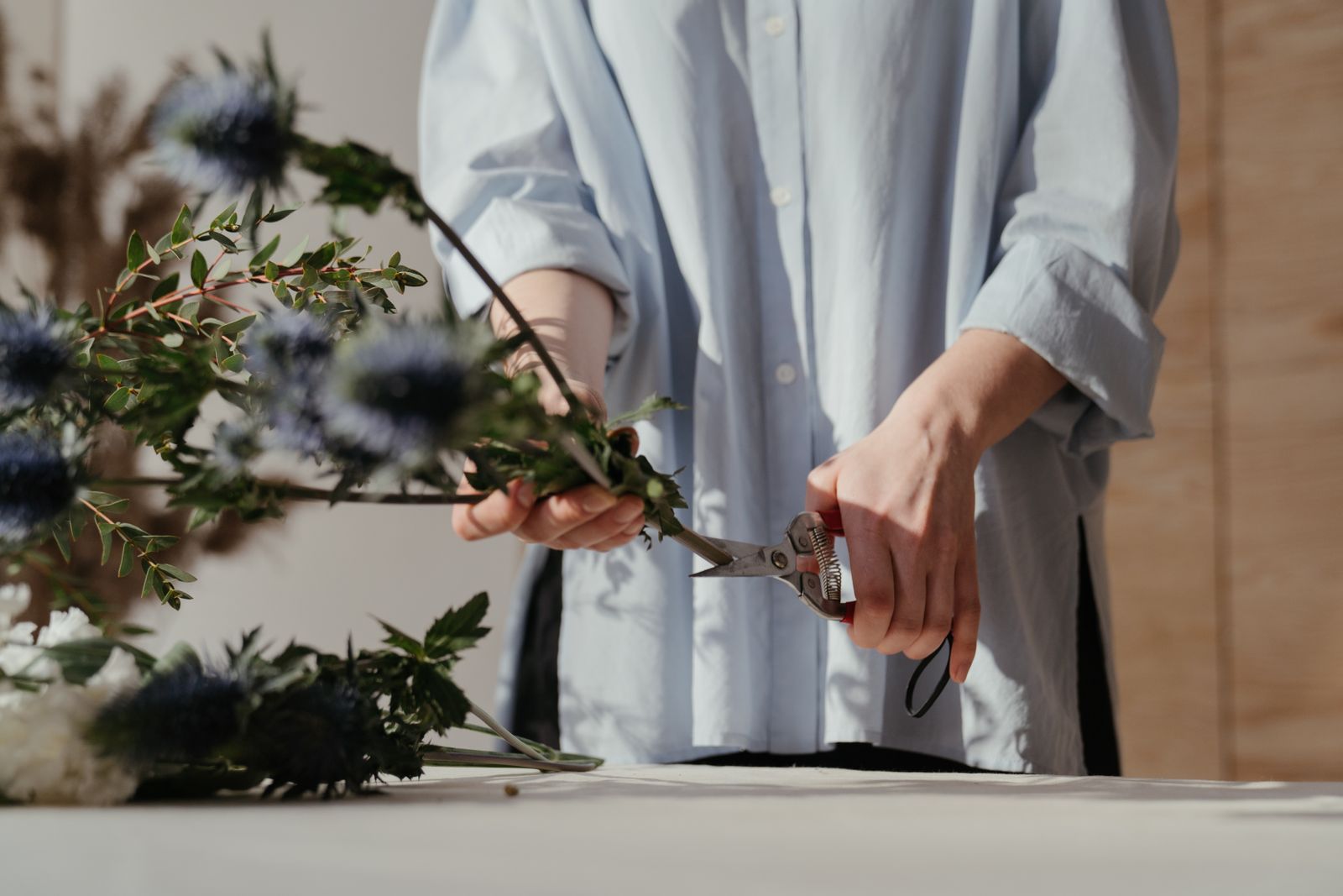 Mains de fleuriste taillant les tiges à l'établi