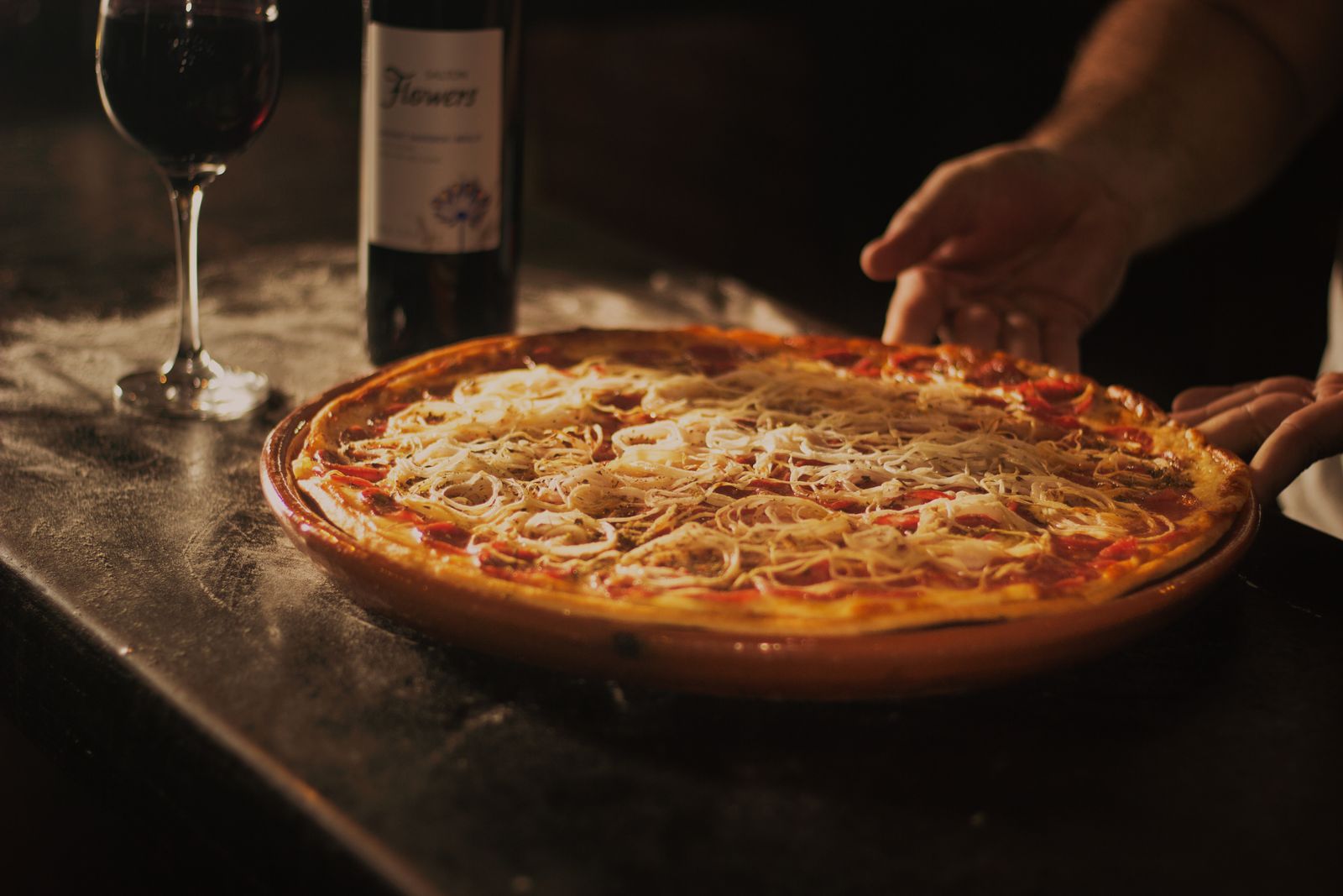 Pizza servie sur la grande table en bois, un verre de vin rouge à côté