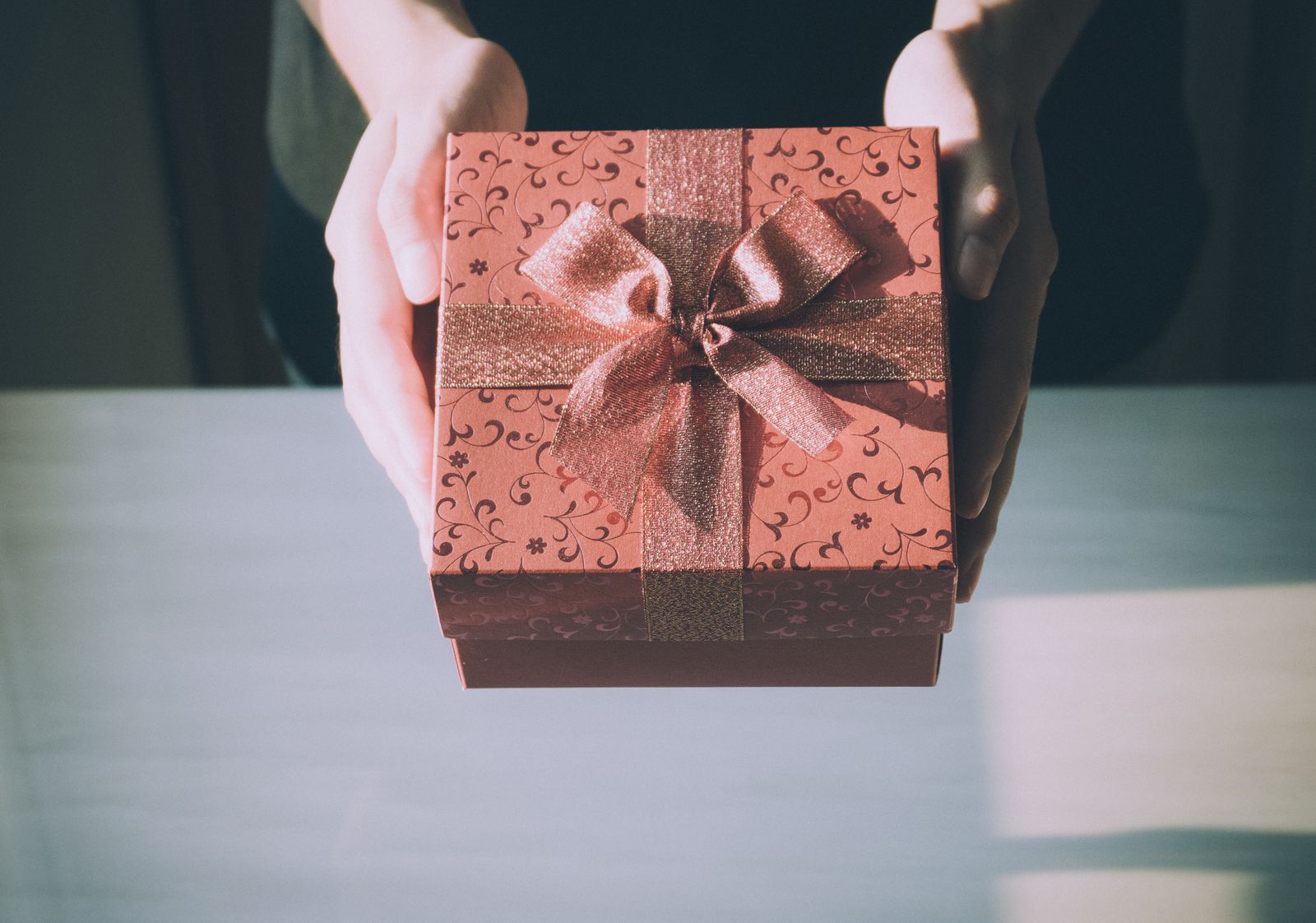 Des mains tendant un paquet cadeau noué d'un ruban